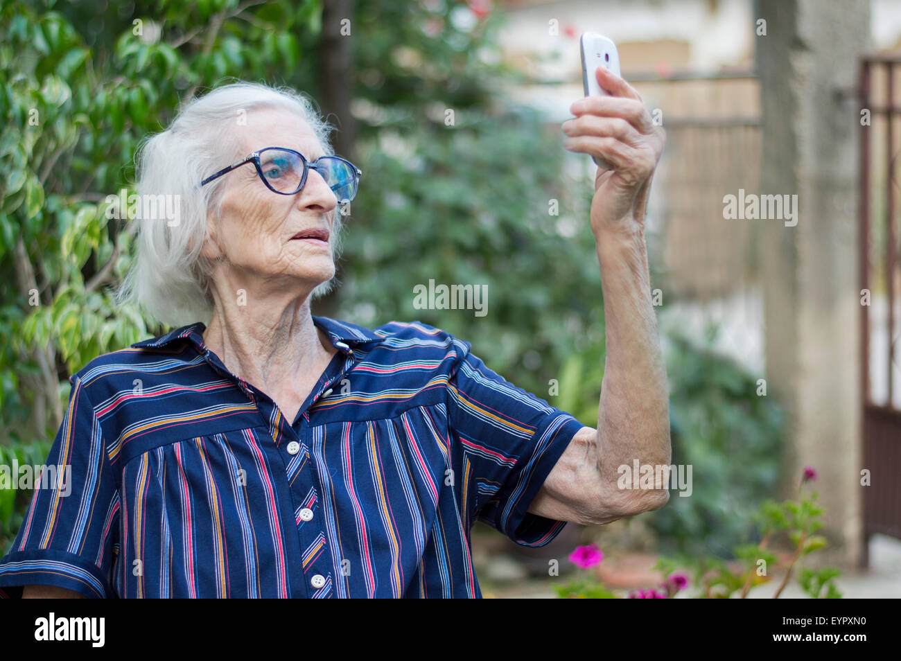 Ninety years old grandma taking a selfie with a smartphone in the backyard. Communications abstract Stock Photo