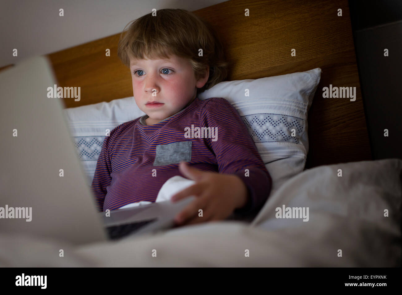 Tired young boy in the evening in bed with notebook. Stock Photo