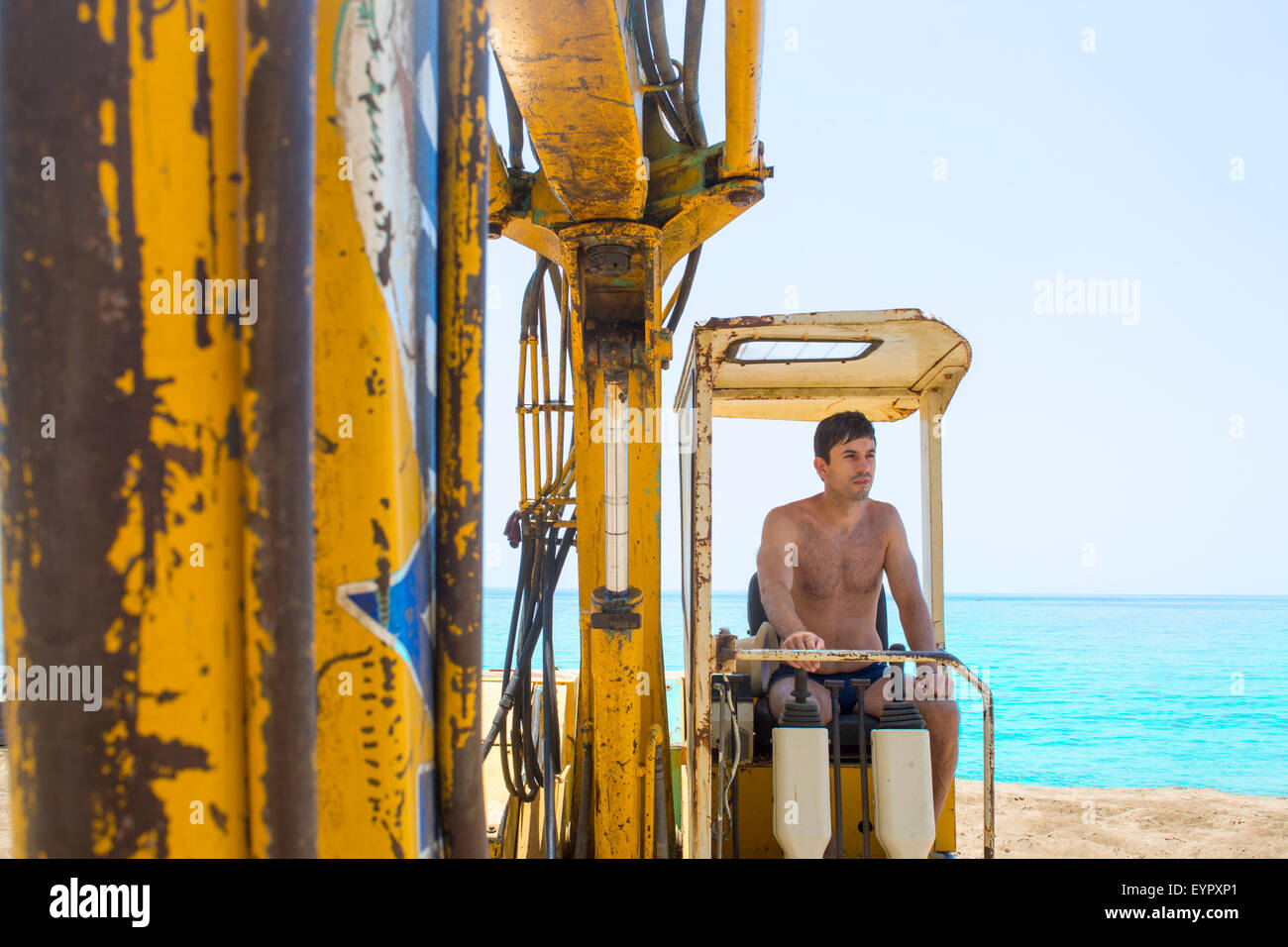 Young man operating the bulldozer at the beach on a hot summer day Stock Photo