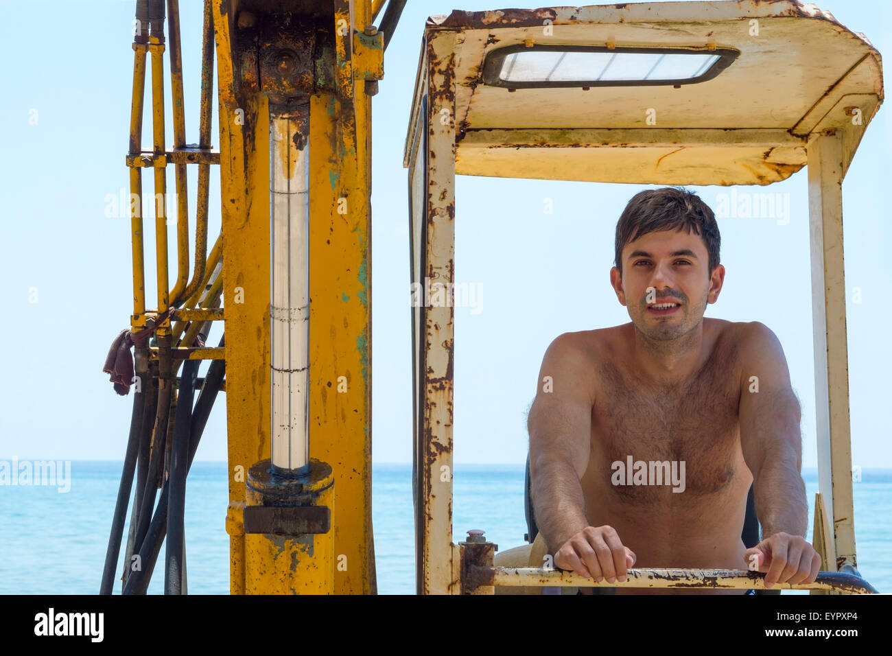 Young man sitting in a bulldozer at the beach on a hot summer day Stock Photo