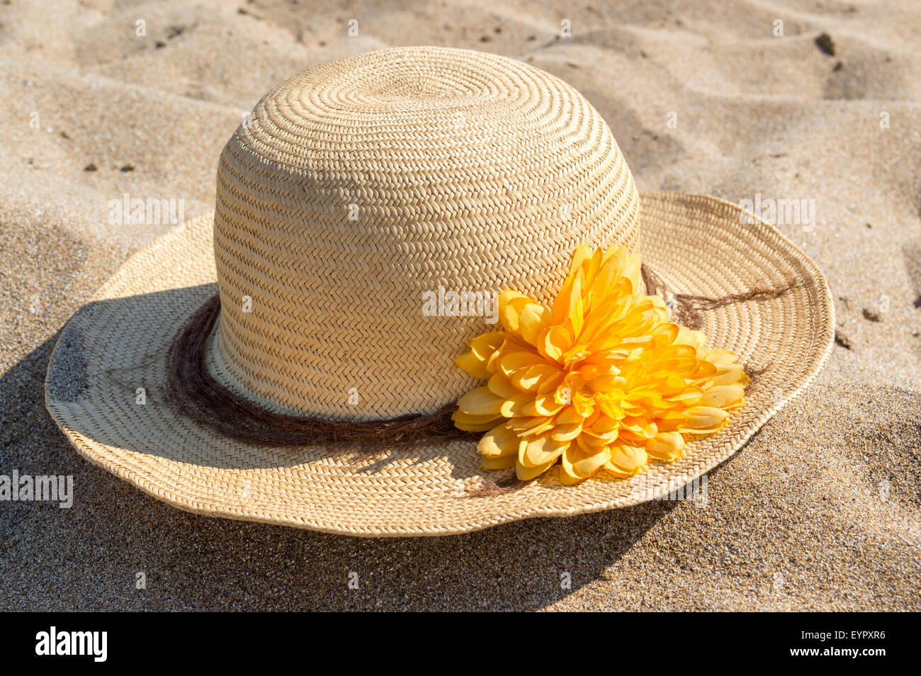 Straw hat with frangipani flowers on white sea sand. With