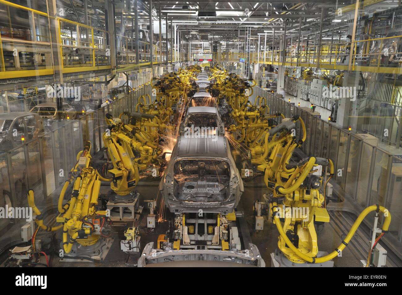Inside a modern car factory, vehicles and parts move through the production process, robots weld row of body shells Stock Photo
