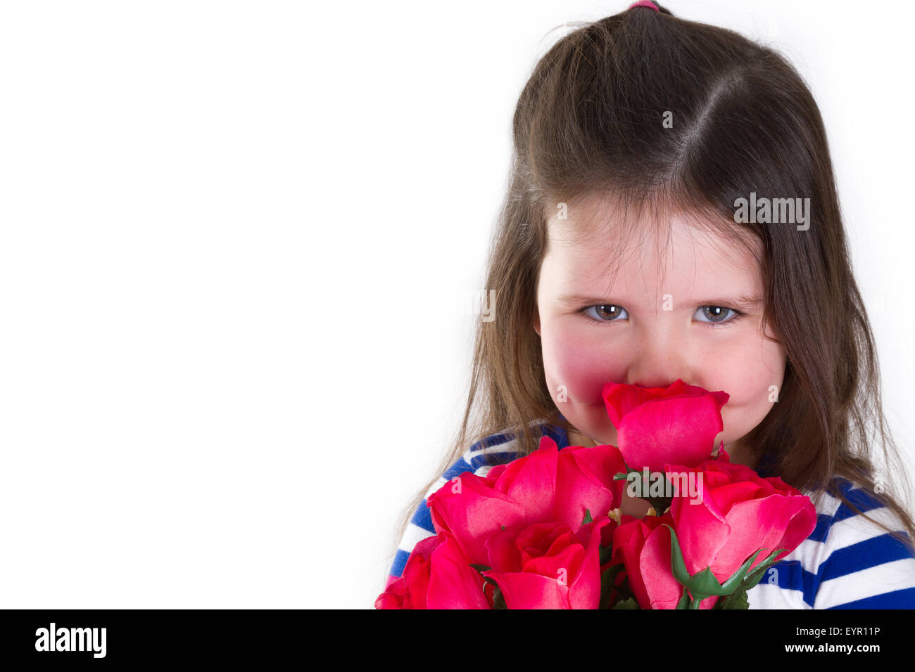 Young girl holding a bunch of artificial roses smelling them. Looking at the camera and lots of copy space. Stock Photo