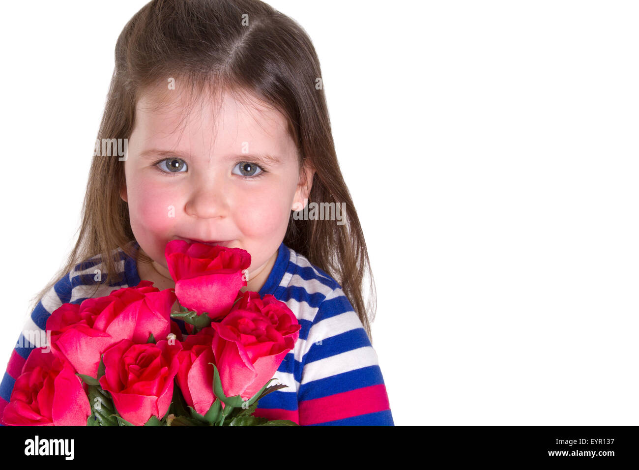Young girl holding a bunch of artifiical roses smelling them. Looking at the camera and lots of copy space. Stock Photo