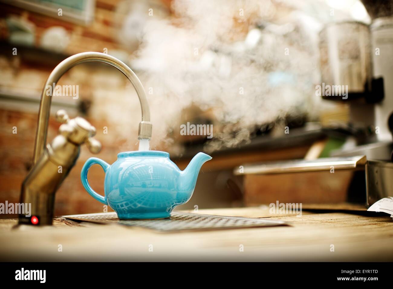 Blue traditional English tea pot being filled with steaming boiling