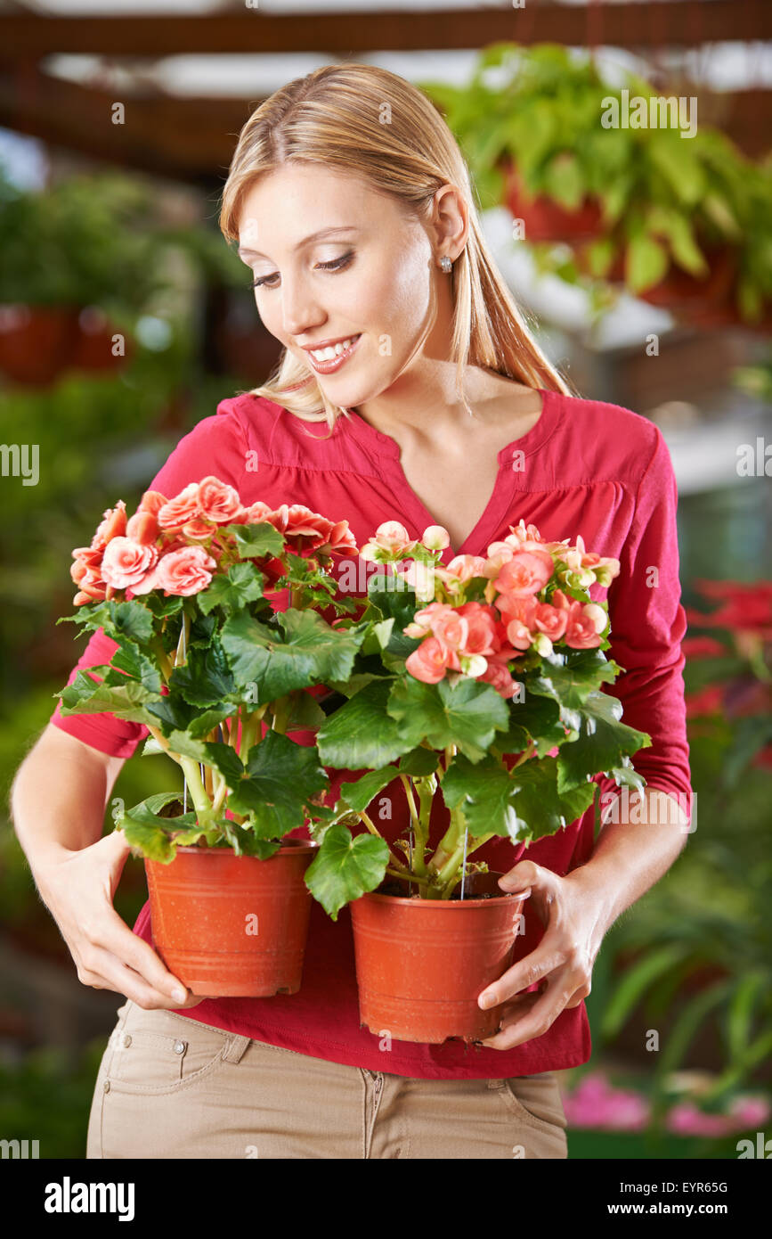Smiling woman holding two begonia flowers in garden center Stock Photo