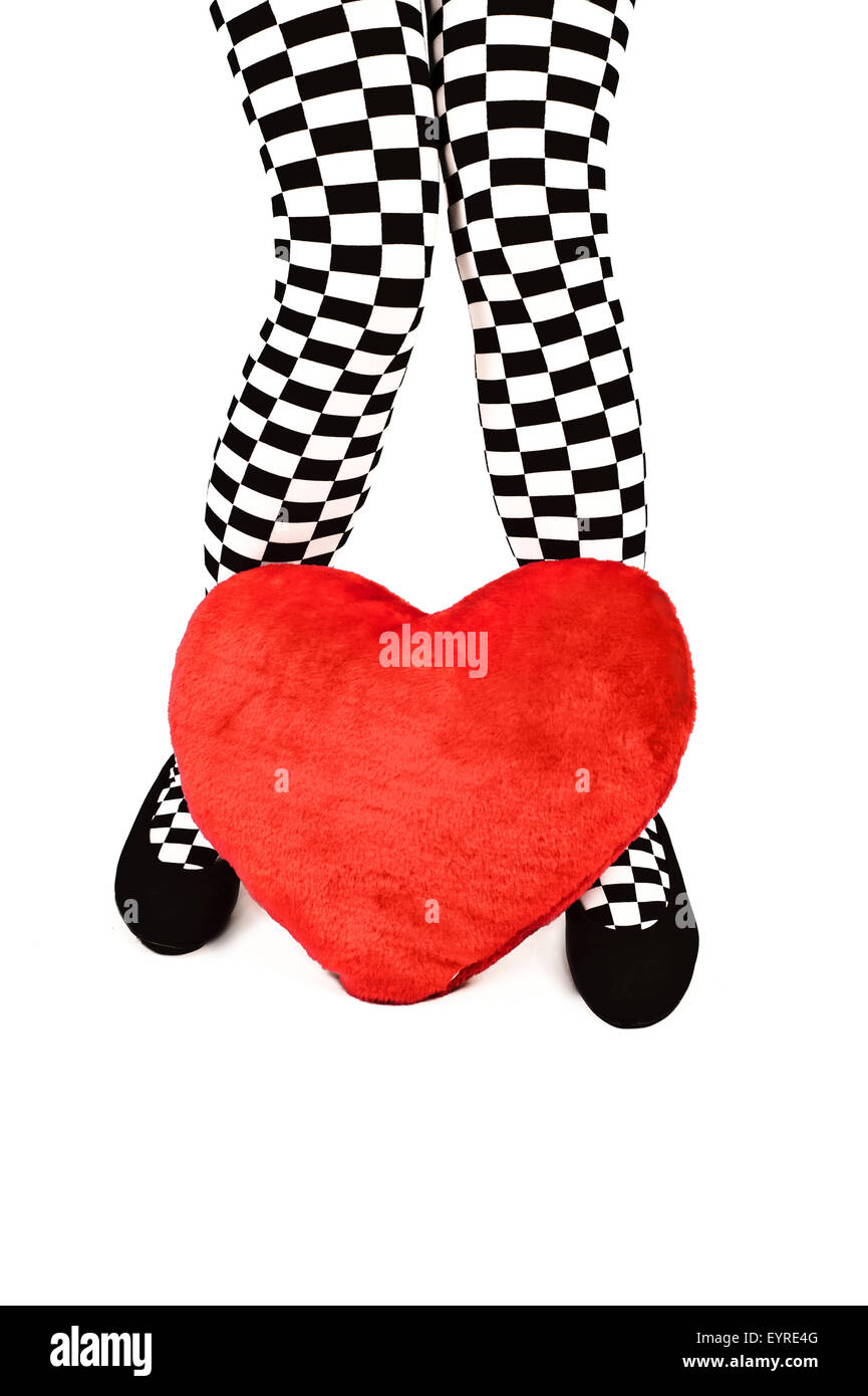 legs of a woman in checkered knee high socks and a red heart shaped cushion Stock Photo