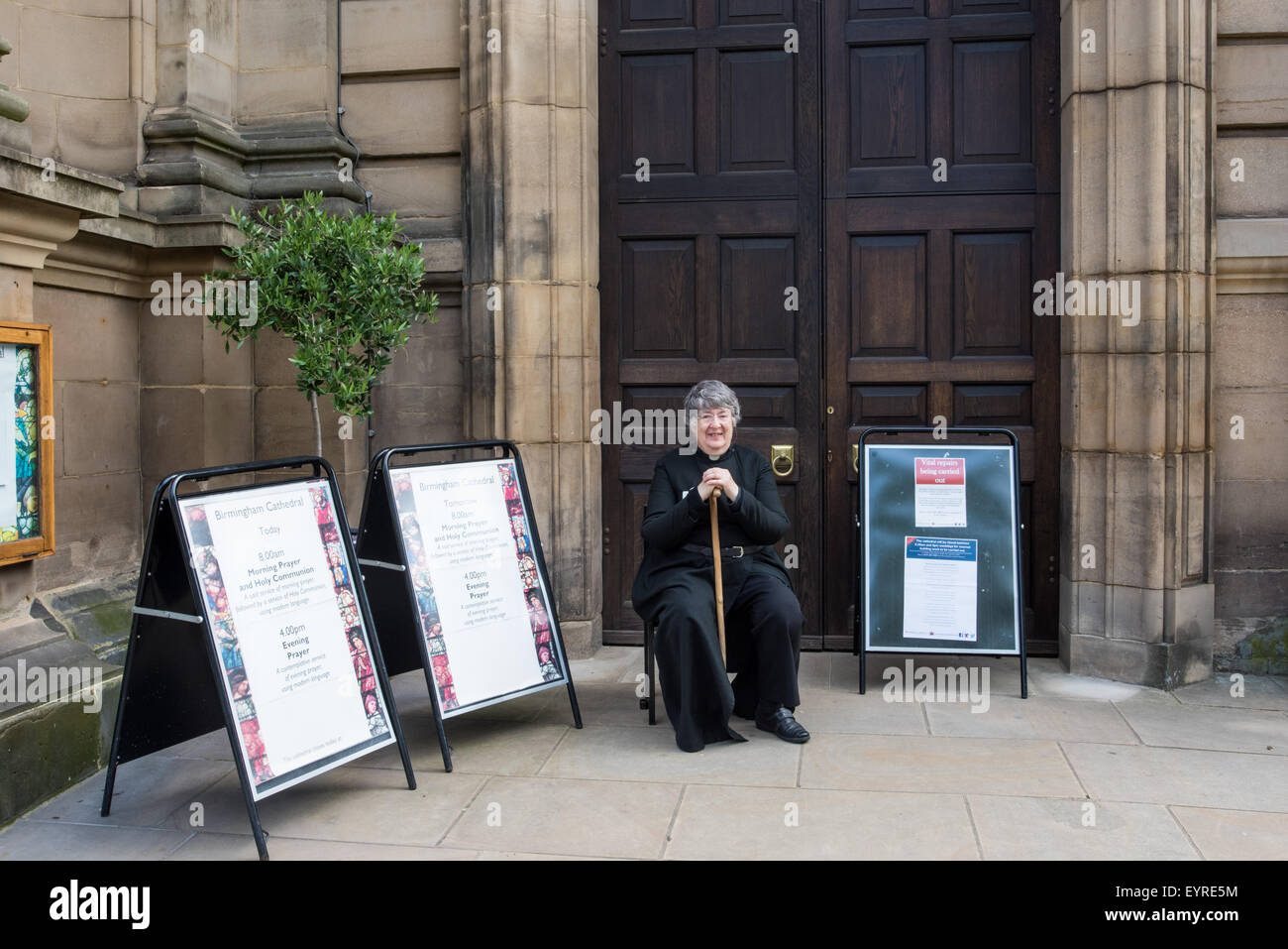 A Female Vicar sat outside Birmingham Cathedral with her walking stick West Midlands UK Stock Photo