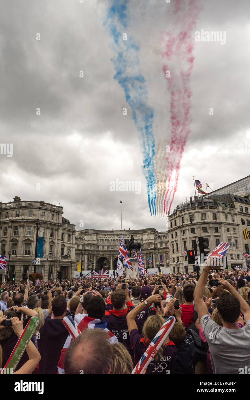 Trafagar Square, London, Engand. The red arrows fly past streaming red white and blue over the crowds with Union Jack flags. Stock Photo