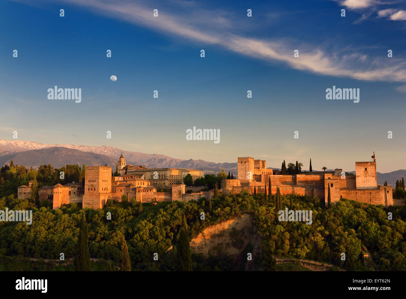 Moon and golden sunset on hilltop Alhambra Palace fortress complex Granada Spain with snow capped Sierra Nevada mountains Stock Photo