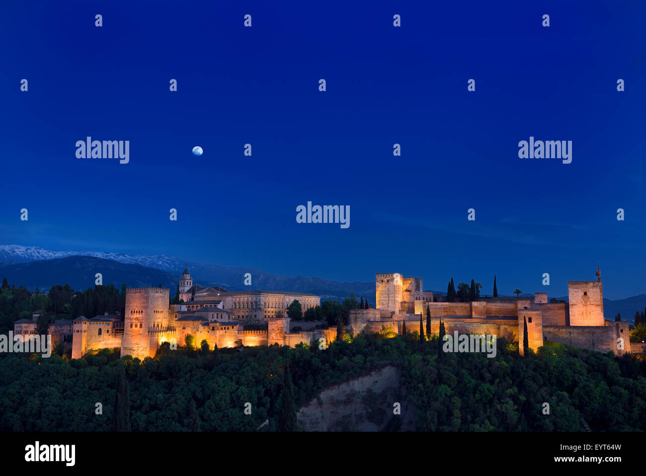 Indigo sky and moonrise over lit hilltop Alhambra Palace fortress complex at twilight Granada Spain Stock Photo