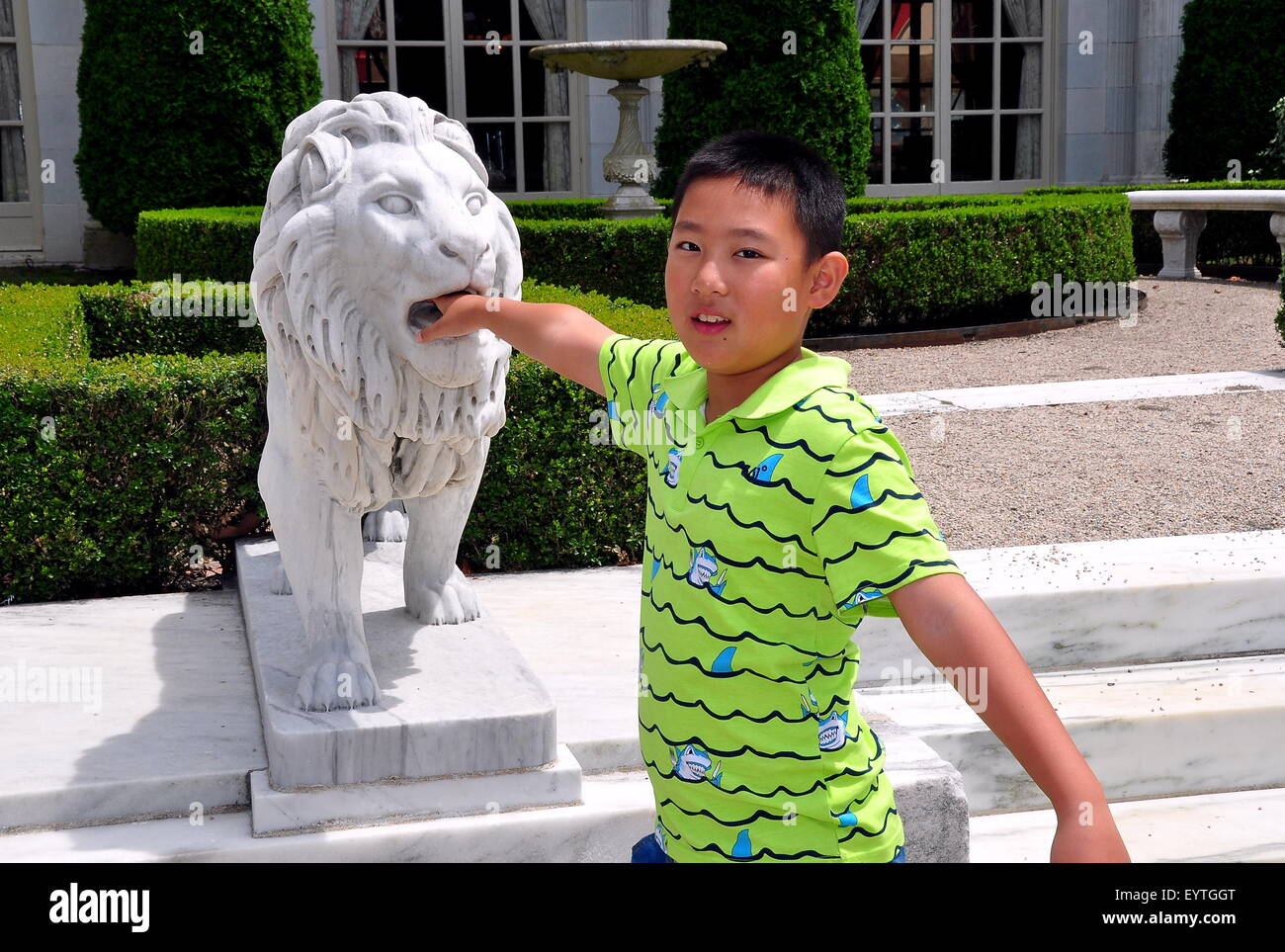 Newport, RI:  Little Chinese boy puts his hand into the mouth of a carved lion in front of  1898-1902 Rosecliff Mansion Stock Photo