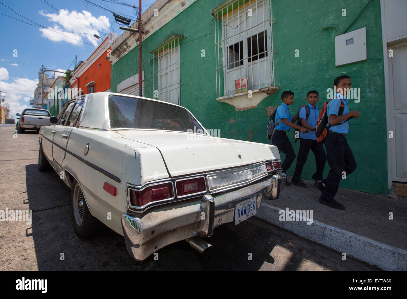 Old wreck car parked in the old colonial city of Ciudad Bolivar with kids walking back from the school. Venezuela Stock Photo