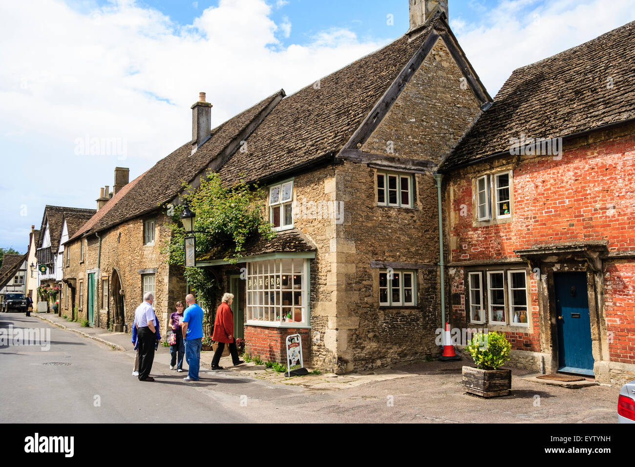 England, Lacock, Cotswolds. Church Street, 15th century - 18th century Cotswold stone houses and village bakery. People in street, sunshine. Stock Photo