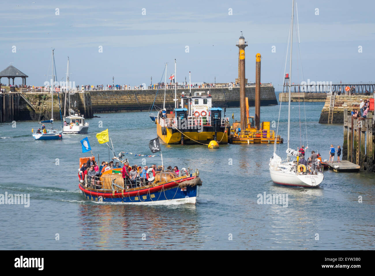 Crowded Whitby harbour with the  Lifeboat 'Mary Ann Hepworth' inbound passing  the dredger “Sandsed” and several sailing craft. Stock Photo