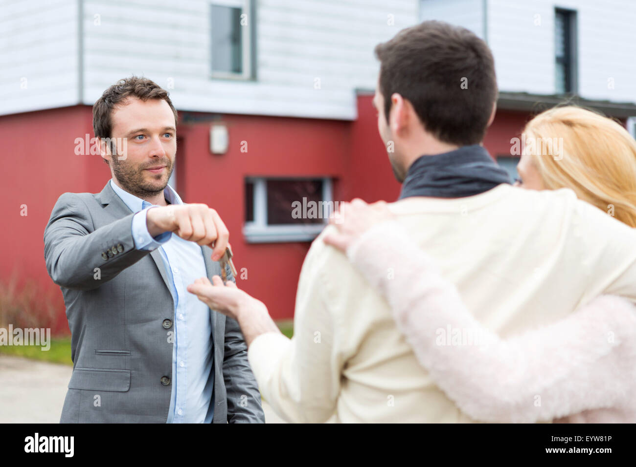 View of a Real estate agent delivers keys to young atractive couple ...