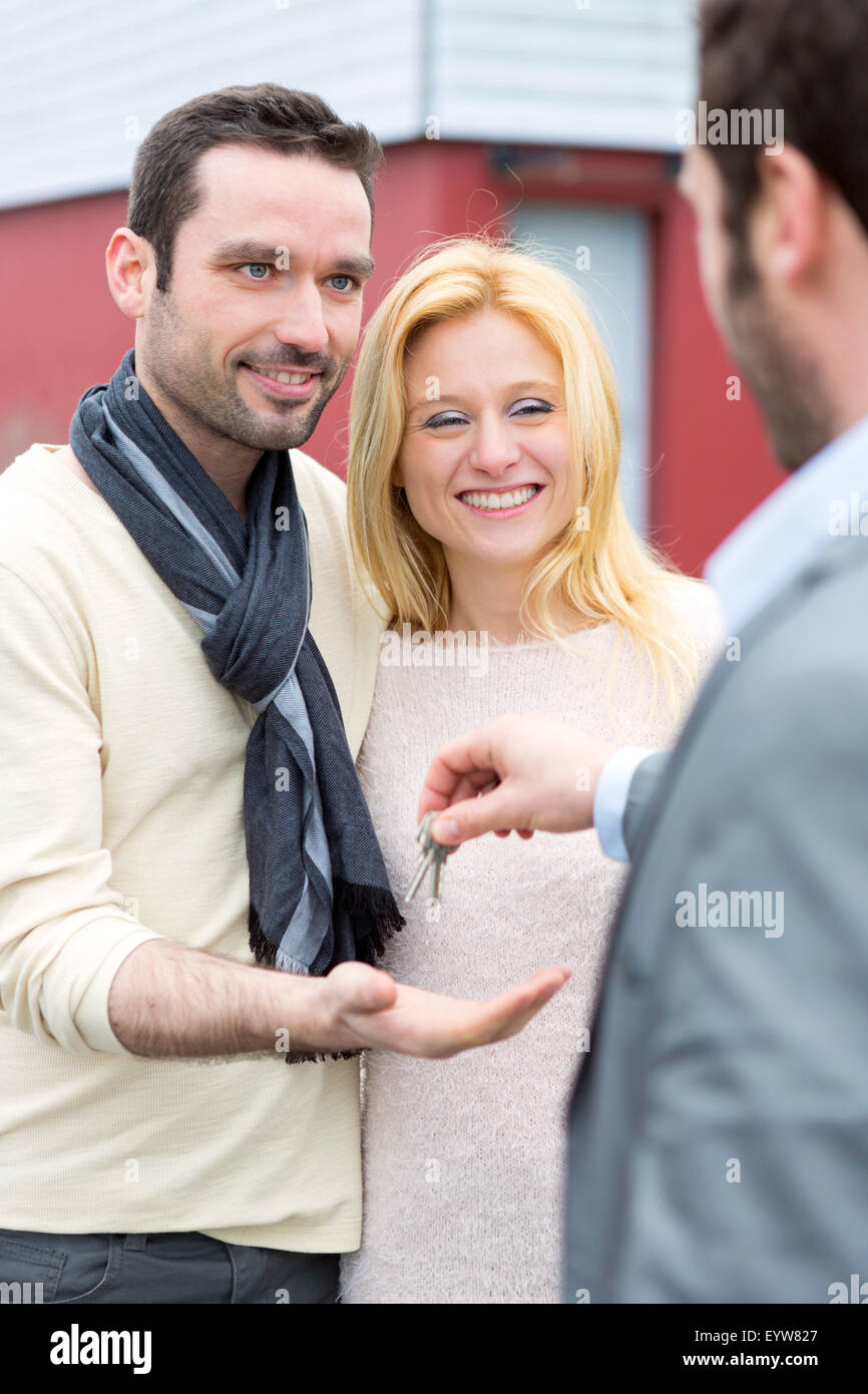 View of a Real estate agent delivers keys to young atractive couple ...