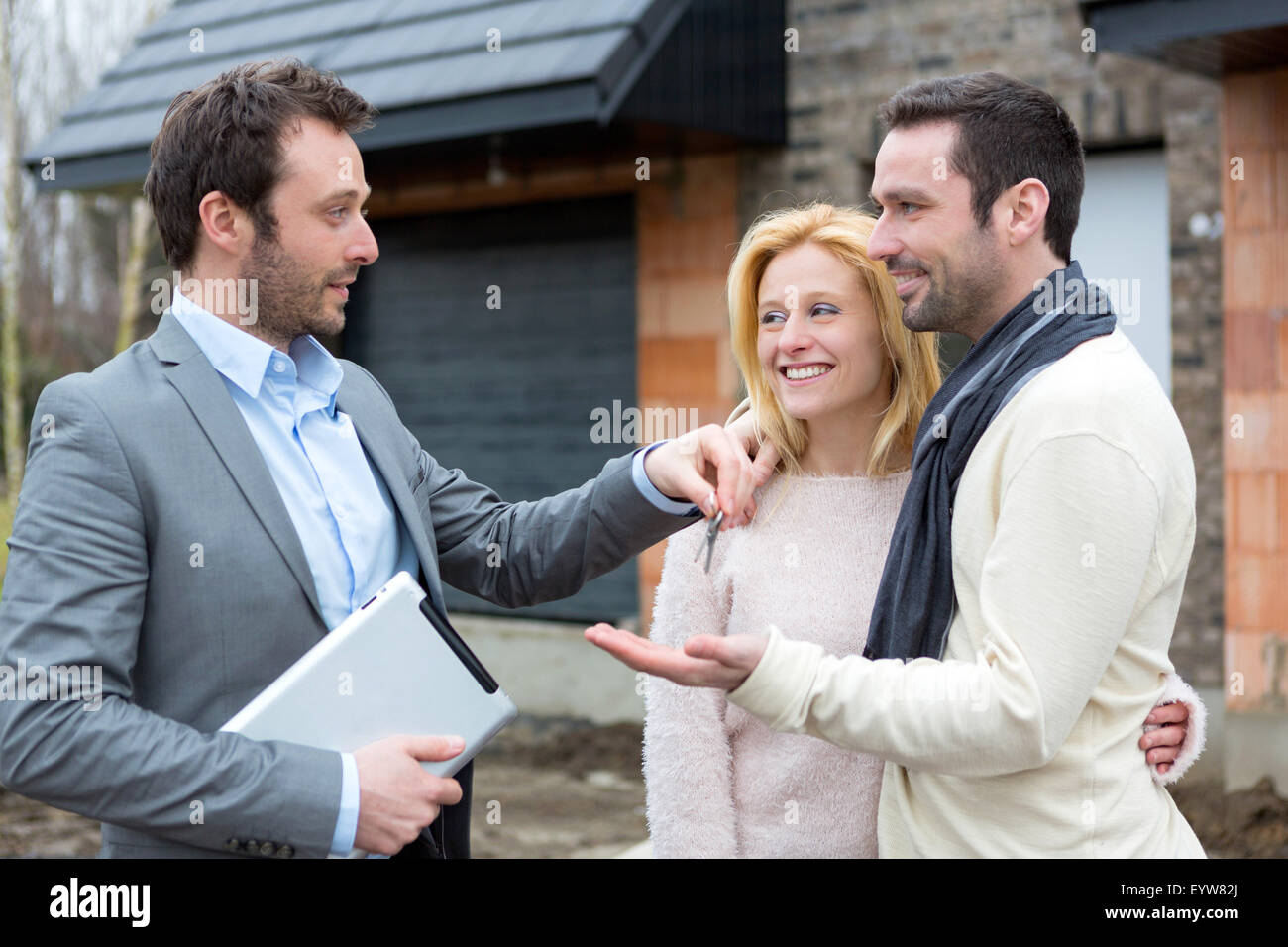 View of a Real estate agent delivers keys to young atractive couple ...