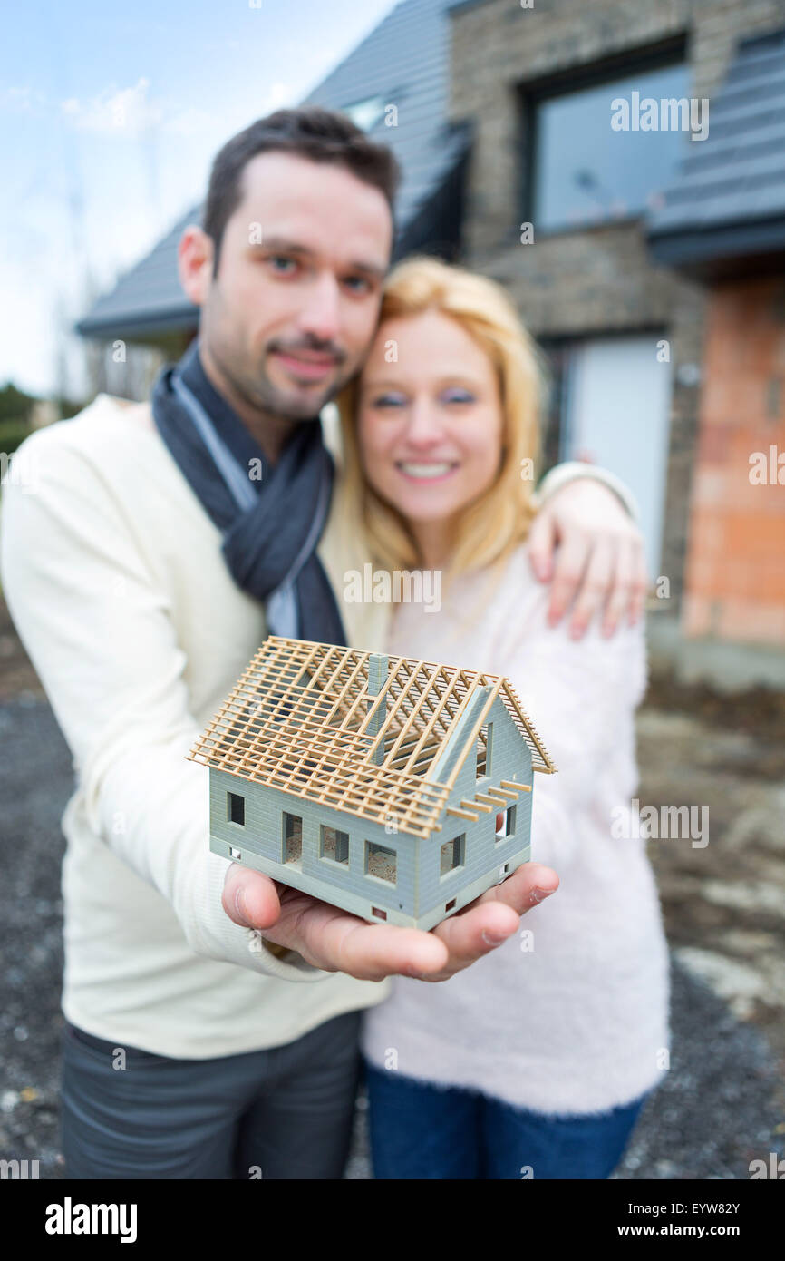 VIew of a Young happy couple handling a miniature house in front of ...
