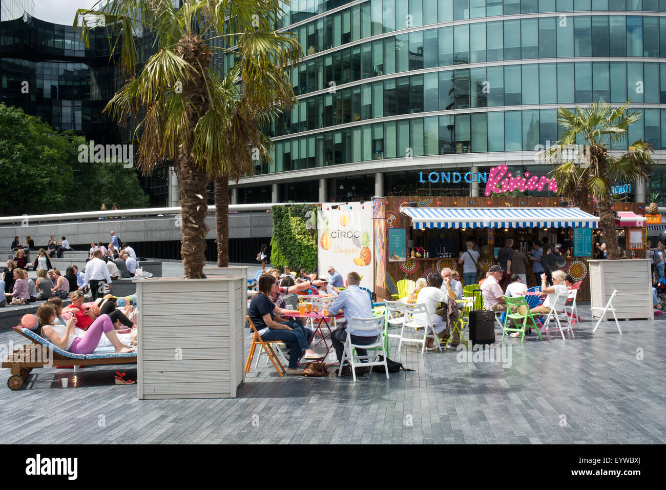 Visitors relax close to City Hall and More London Riverside at the London Riviera café on the South Bank of the River Thames. Stock Photo