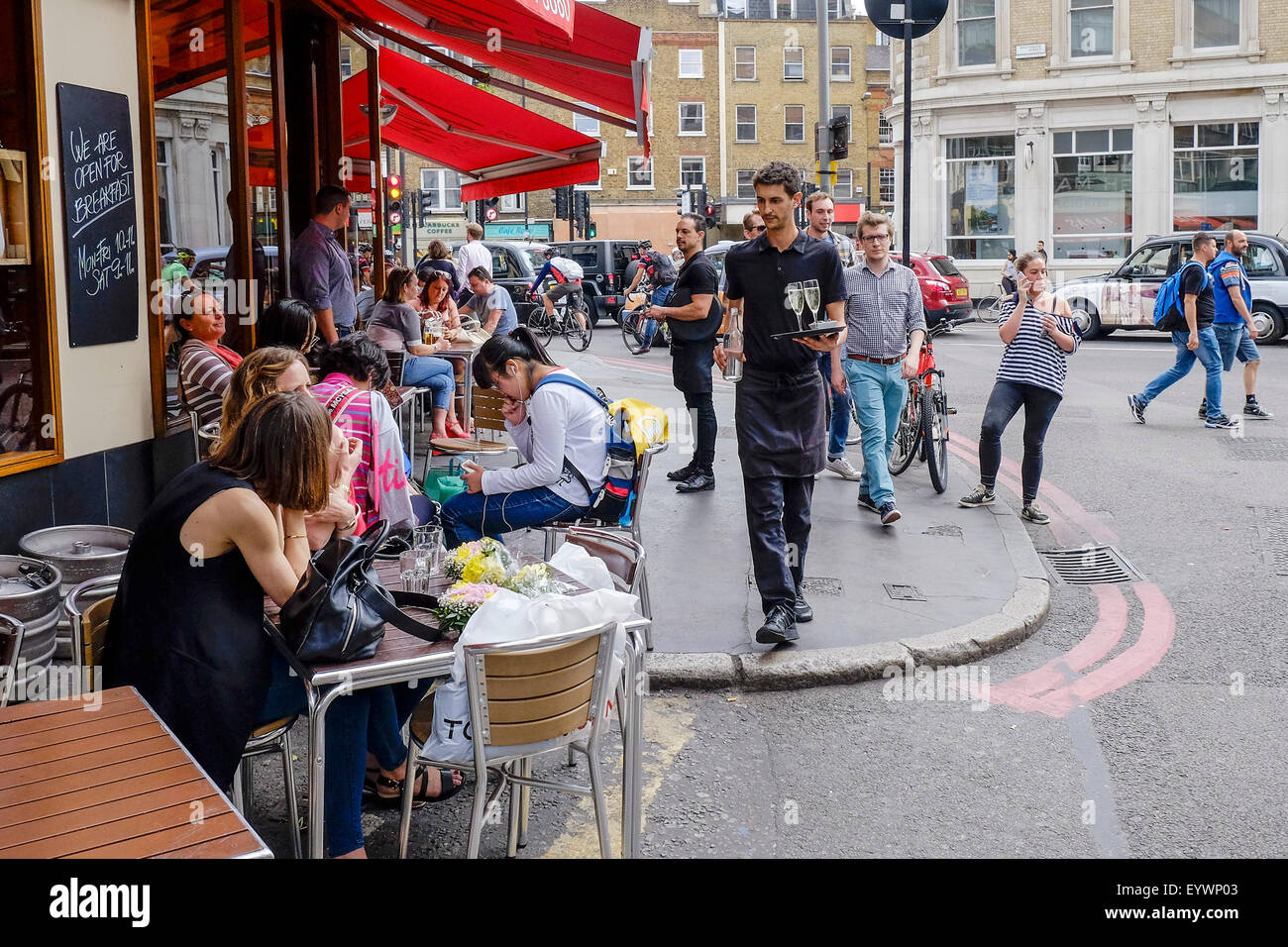 A waiter serving tourists sitting outside a cafe in a street in Southwalk, London. Stock Photo