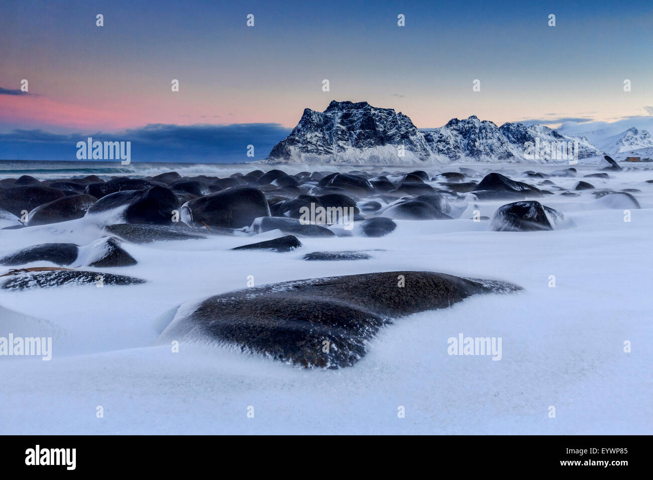 The cold wind that blows constantly shapes the snow on the rocks around Uttakleiv at dawn, Lofoten Islands, Arctic, Norway Stock Photo