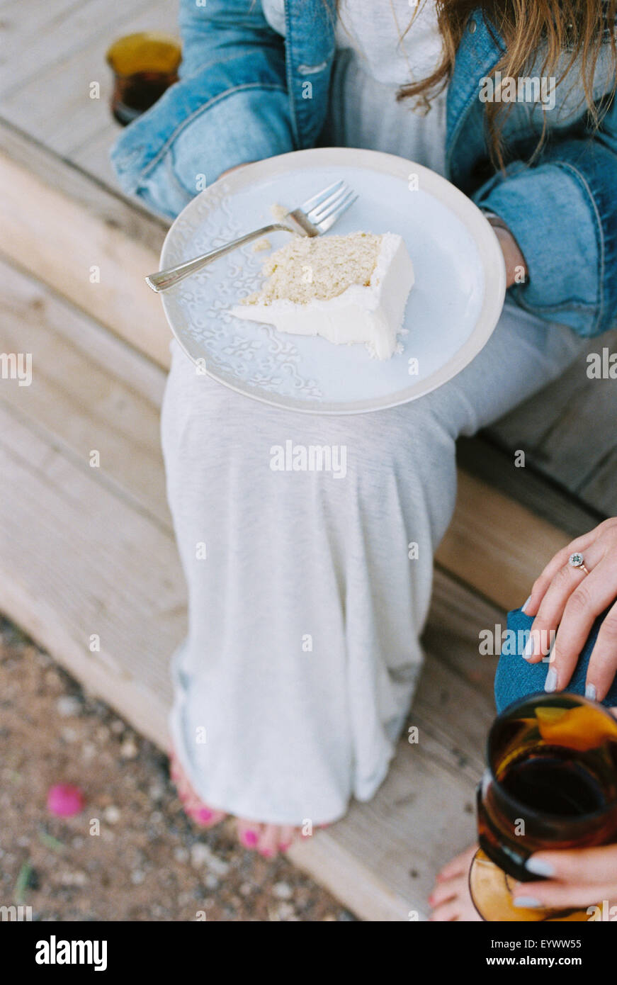 High angle view of a plate with a slice of cake balanced on a woman's knee. Stock Photo
