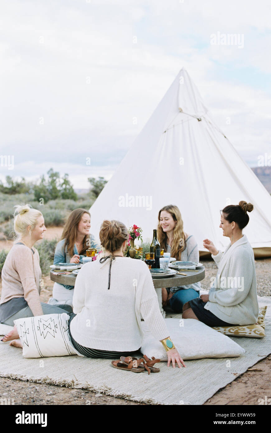 Group of women enjoying an outdoor meal by a teepee in the desert. Stock Photo
