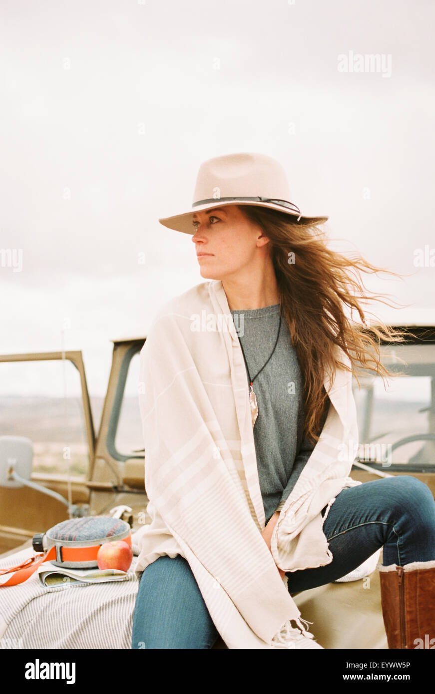 Woman wearing a hat sitting on the front of a jeep looking around her. Stock Photo