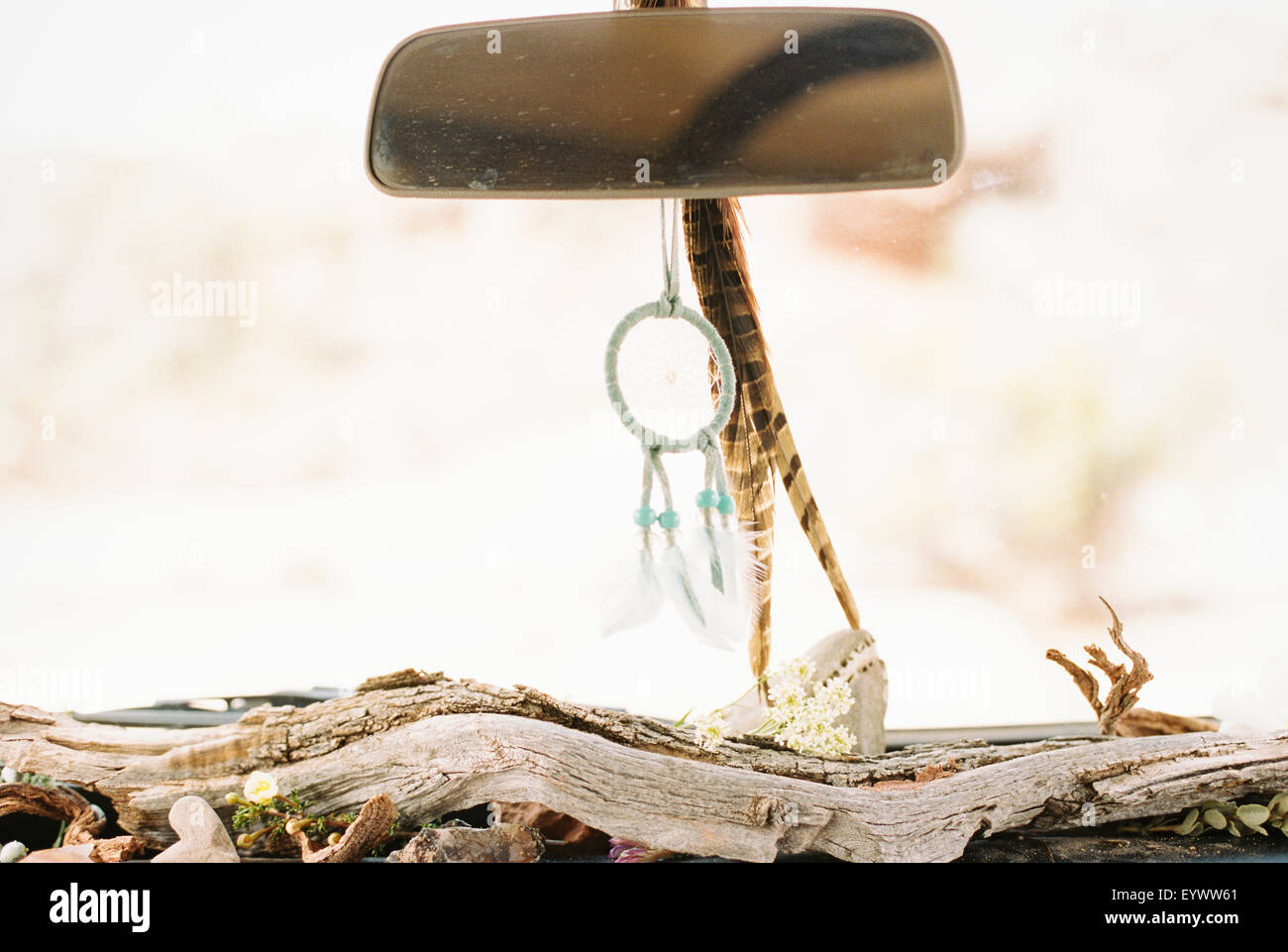 Close up of a car interior, driftwood on the dashboard, a dream catcher and feathers hanging from the rear view mirror. Stock Photo