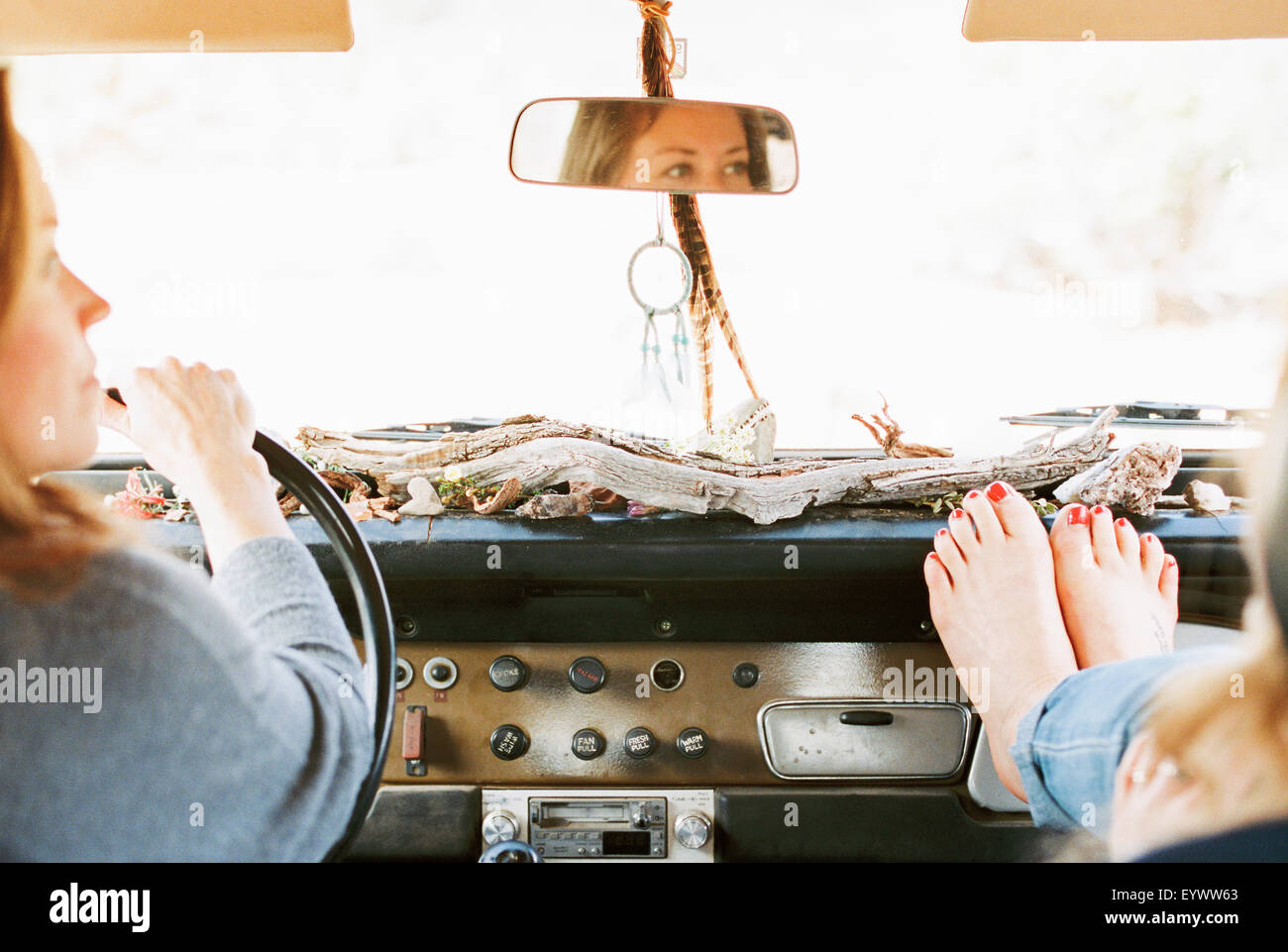 A woman resting her bare feet on the dashboard of a 4x4, on a road trip