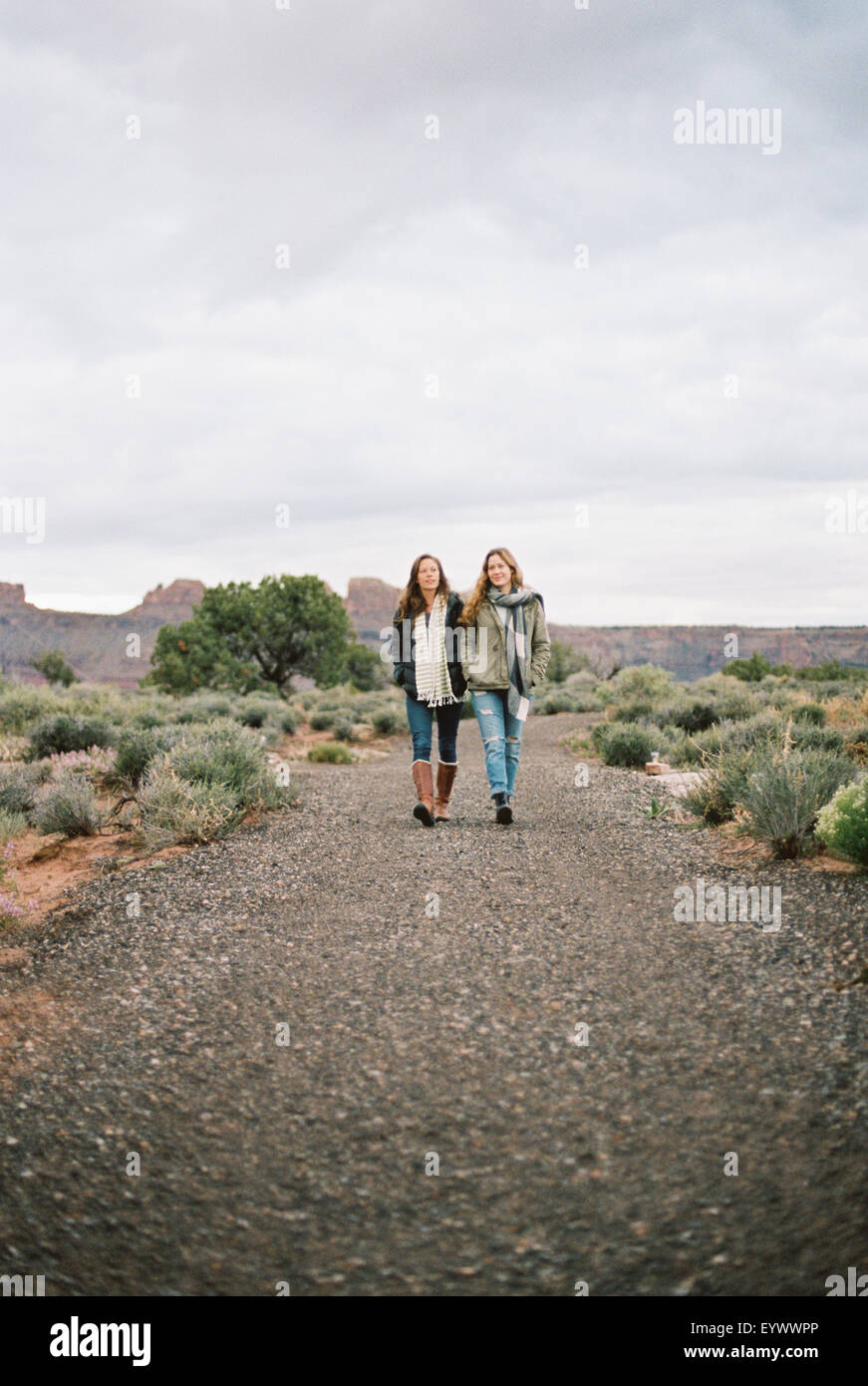 Two women walking down a dirt road in a desert. Stock Photo