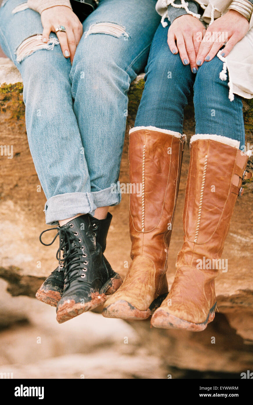 two women wearing leather boots sitting on a rock Stock Photo