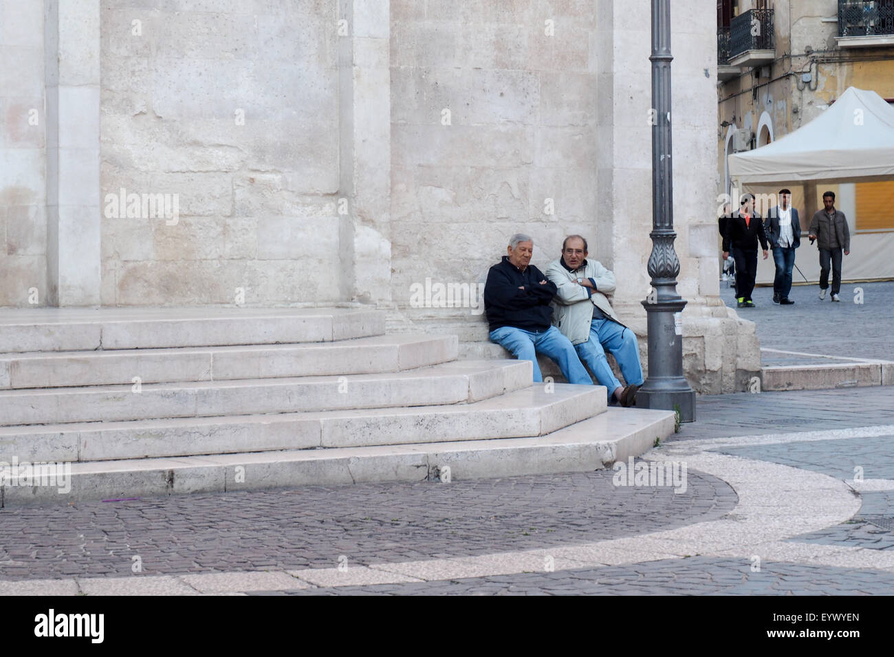 Two men sitting in deep discussion sitting on a ledge in front of Church of Our Lady of the Assumption, Foggia. Stock Photo