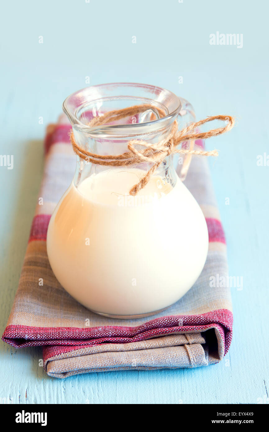 Milk in glass jar on napkin and blue wooden table, vertical Stock Photo
