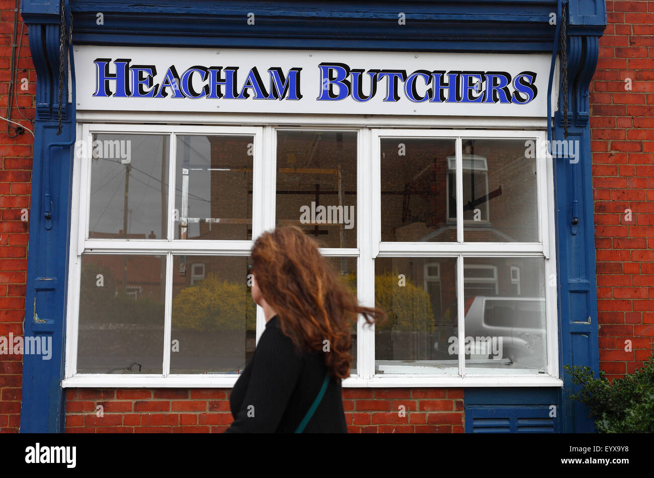 A woman walks past a butcher's shop on a village high street that has closed down. Stock Photo