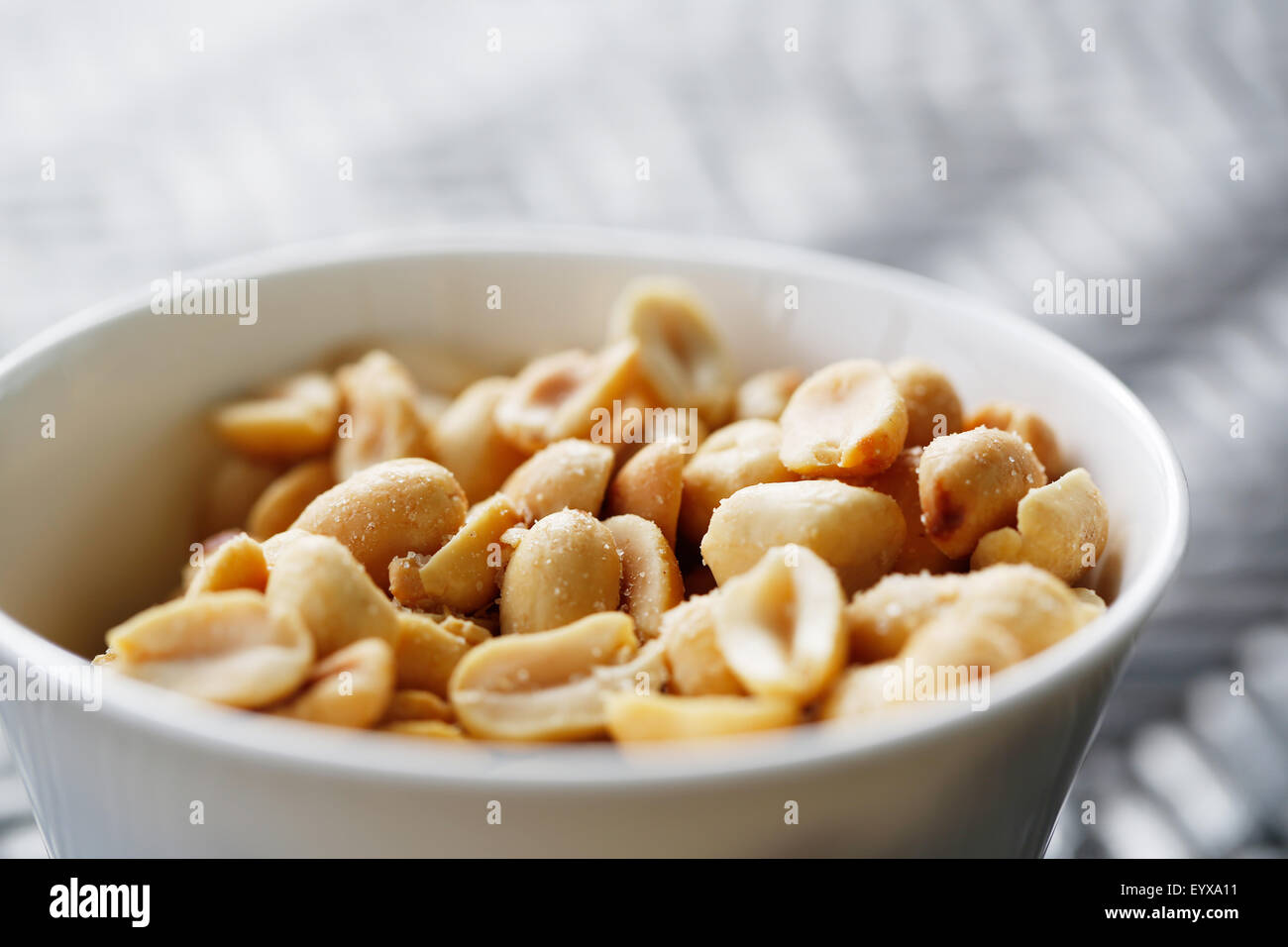 A small bowl of protein but sodium rich roasted salted peanuts presented as a snack in a small white bowl. Stock Photo