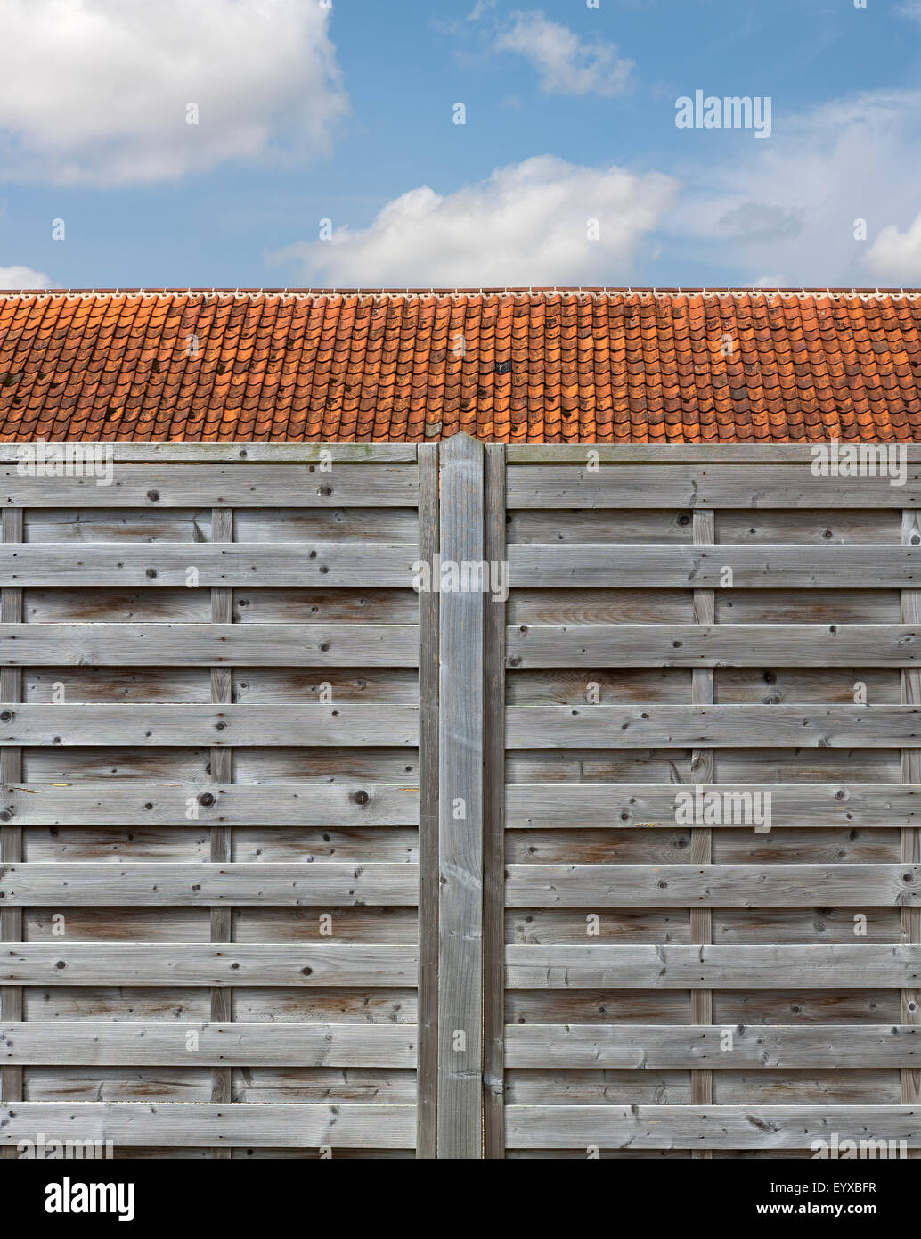 Straight on shot of slatted wooden fence in front of a pantiled roof against a blue lightly clouded sky Norfolk England Stock Photo