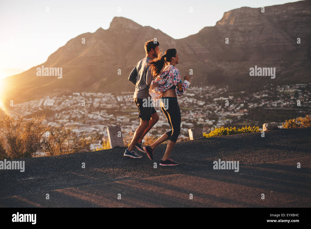 Shot of young man and woman jogging on hillside road. Young couple running in nature. Stock Photo
