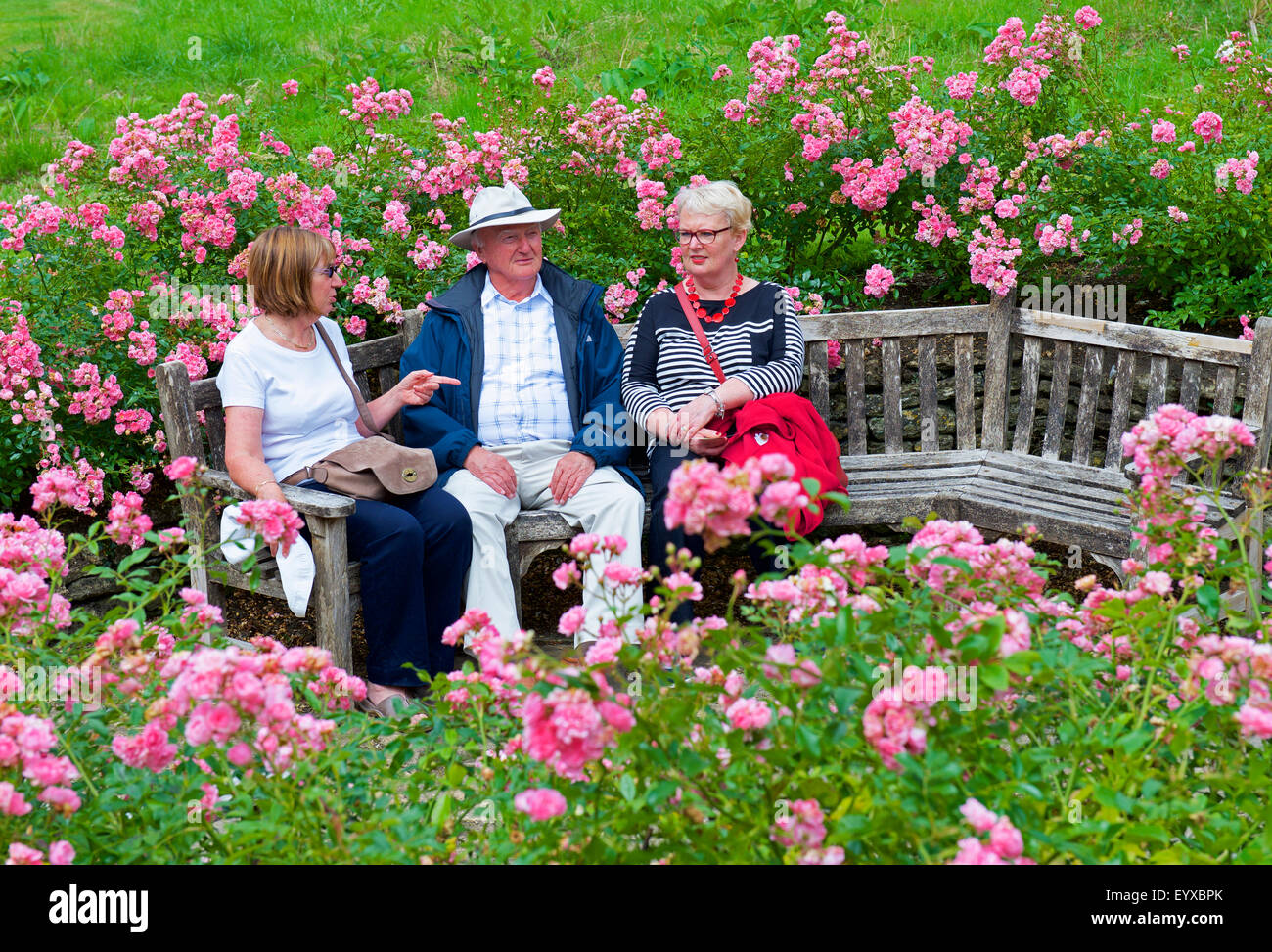 Three people relaxing on bench, Great Chalfield Manor, a National Trust property near Melksham, Wiltshire, England UK Stock Photo