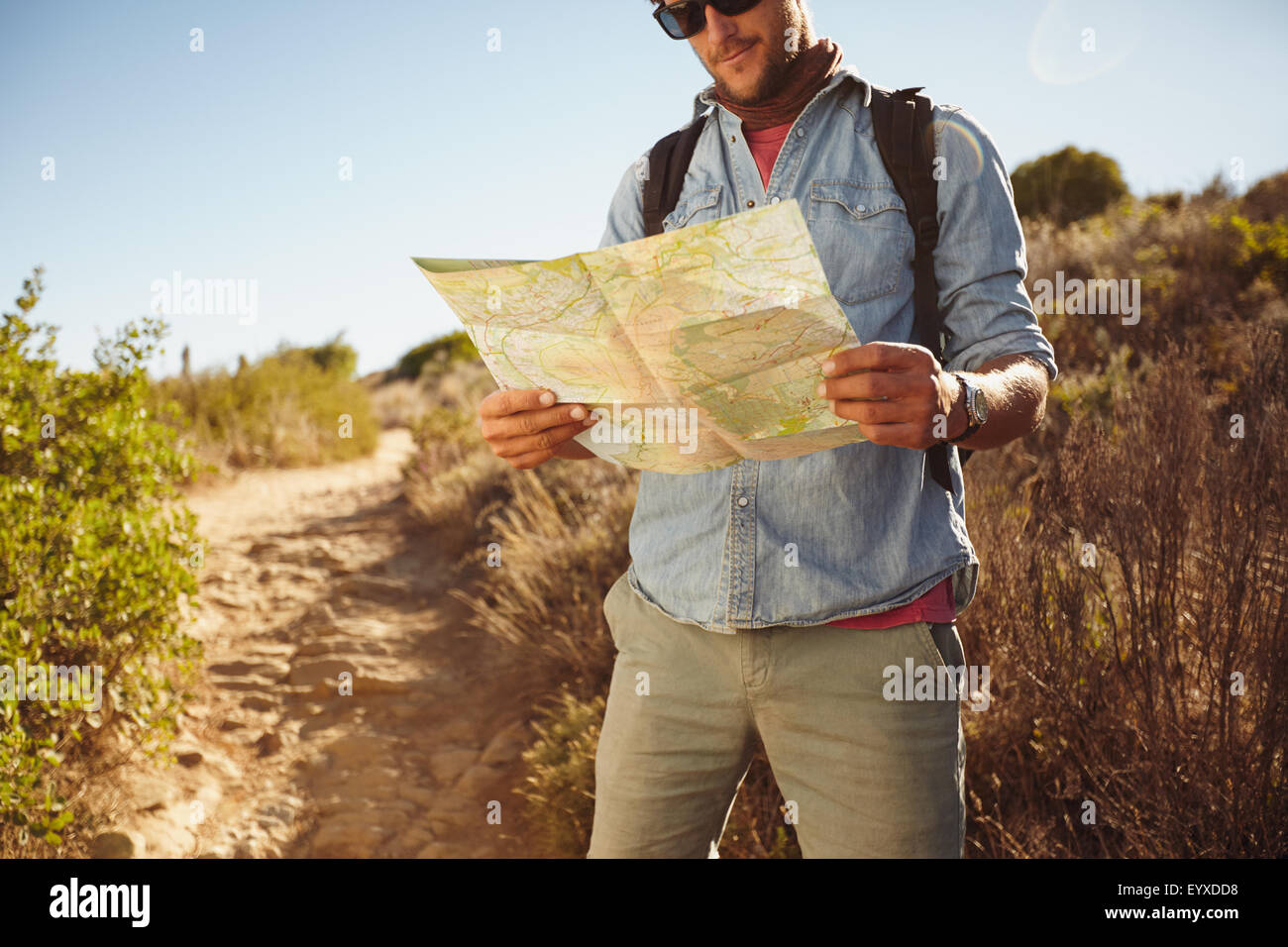 Shot of a man in countryside with a map, figuring out his orientation. Male hiker hiking in country. Stock Photo