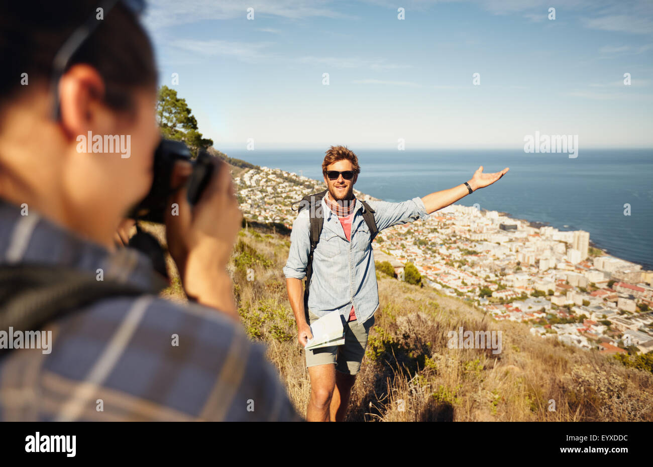 Outdoor shot of tourist couple enjoying nature and taking photo. Woman taking picture of boyfriend showing something with his ha Stock Photo