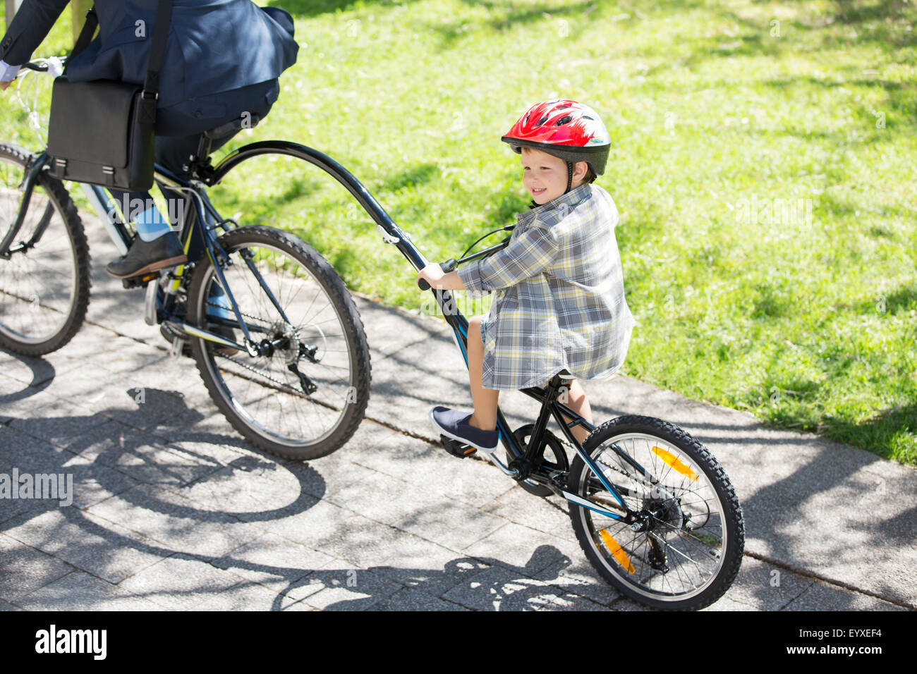 Boy riding tandem bicycle with businessman father in sunny park Stock Photo