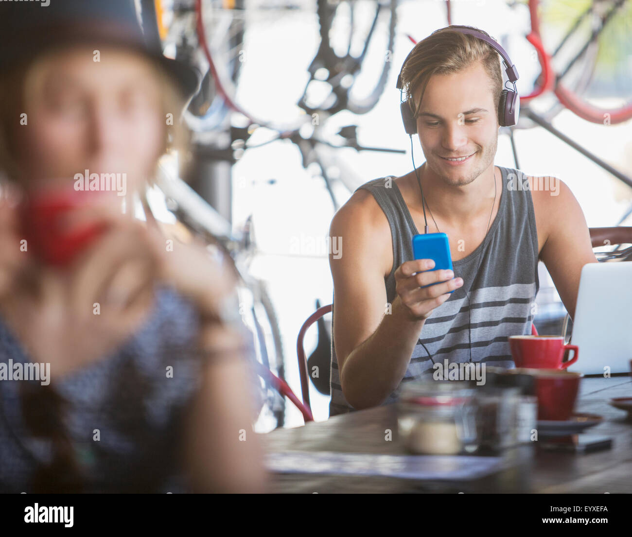 Young man with headphones and laptop texting with cell phone in cafe Stock Photo