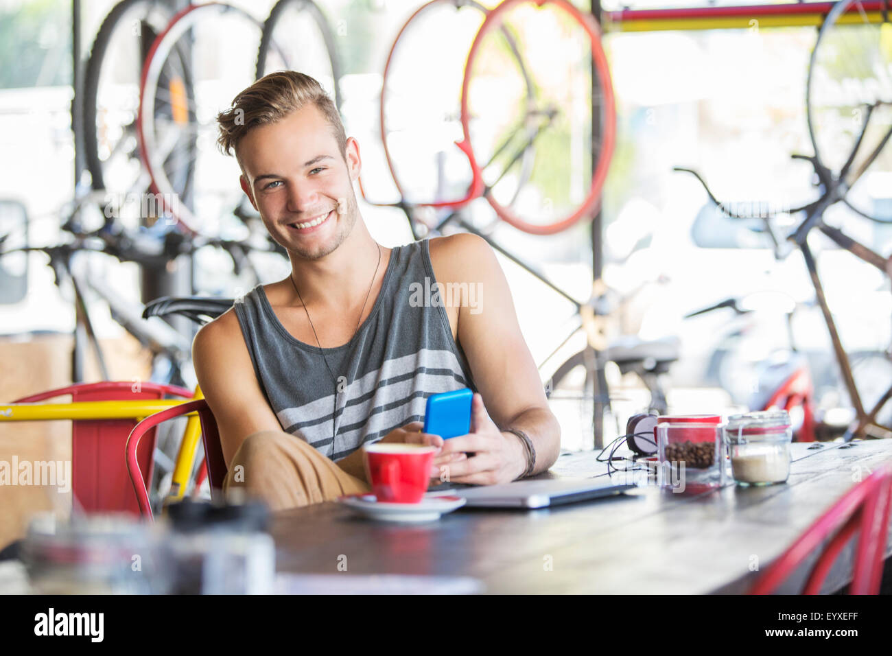 Portrait smiling man with coffee and cell phone in bicycle shop Stock Photo