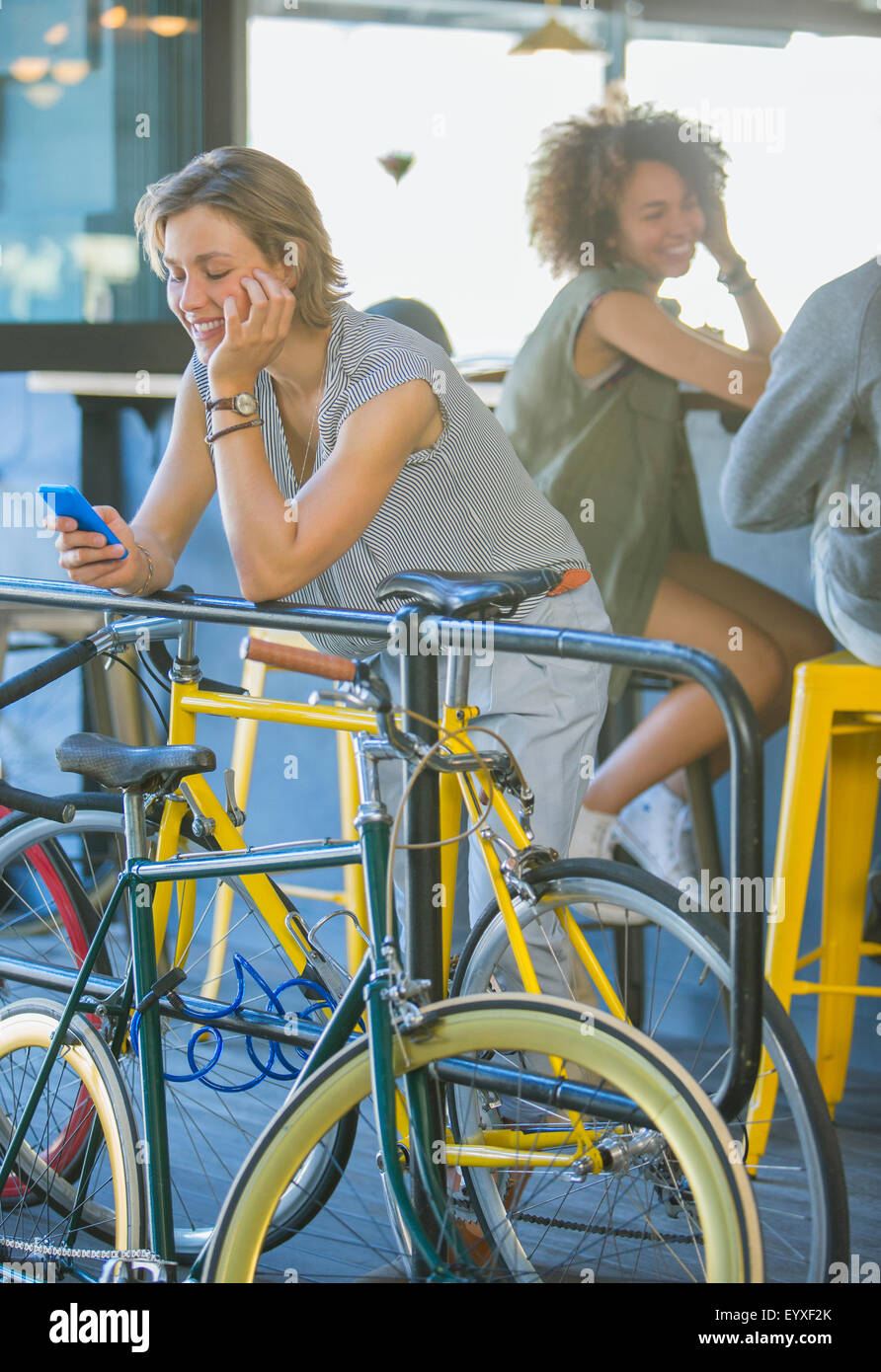 Smiling woman leaning on railing texting with cell phone above bicycle Stock Photo