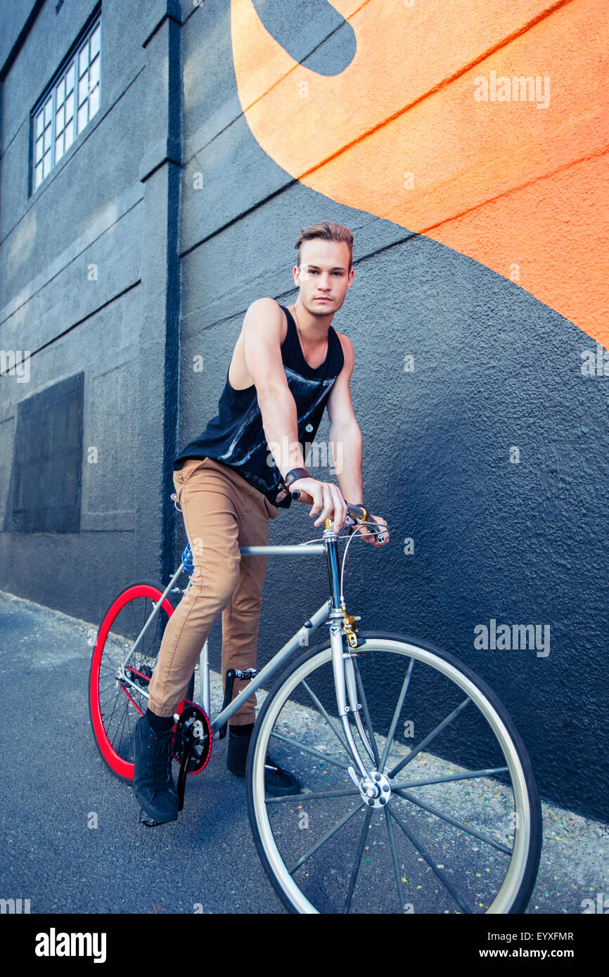 Portrait serious young man on bicycle next to urban graffiti wall Stock Photo