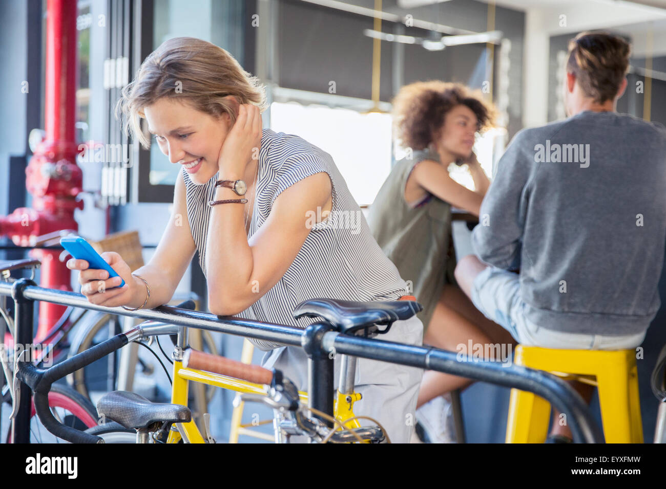 Smiling woman texting with cell phone at railing above bicycle Stock Photo