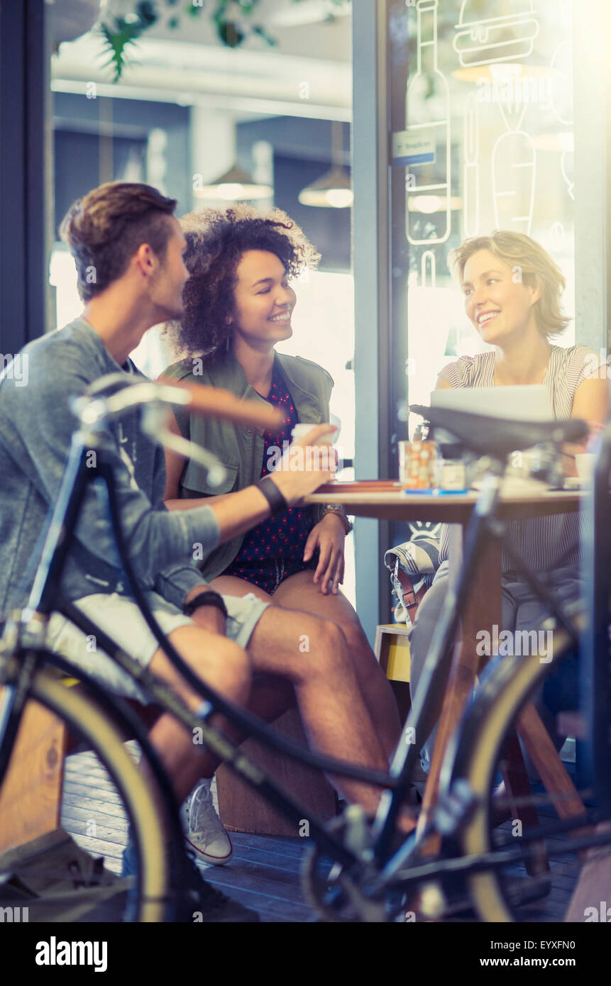 Friends hanging out at cafe table behind bicycle Stock Photo