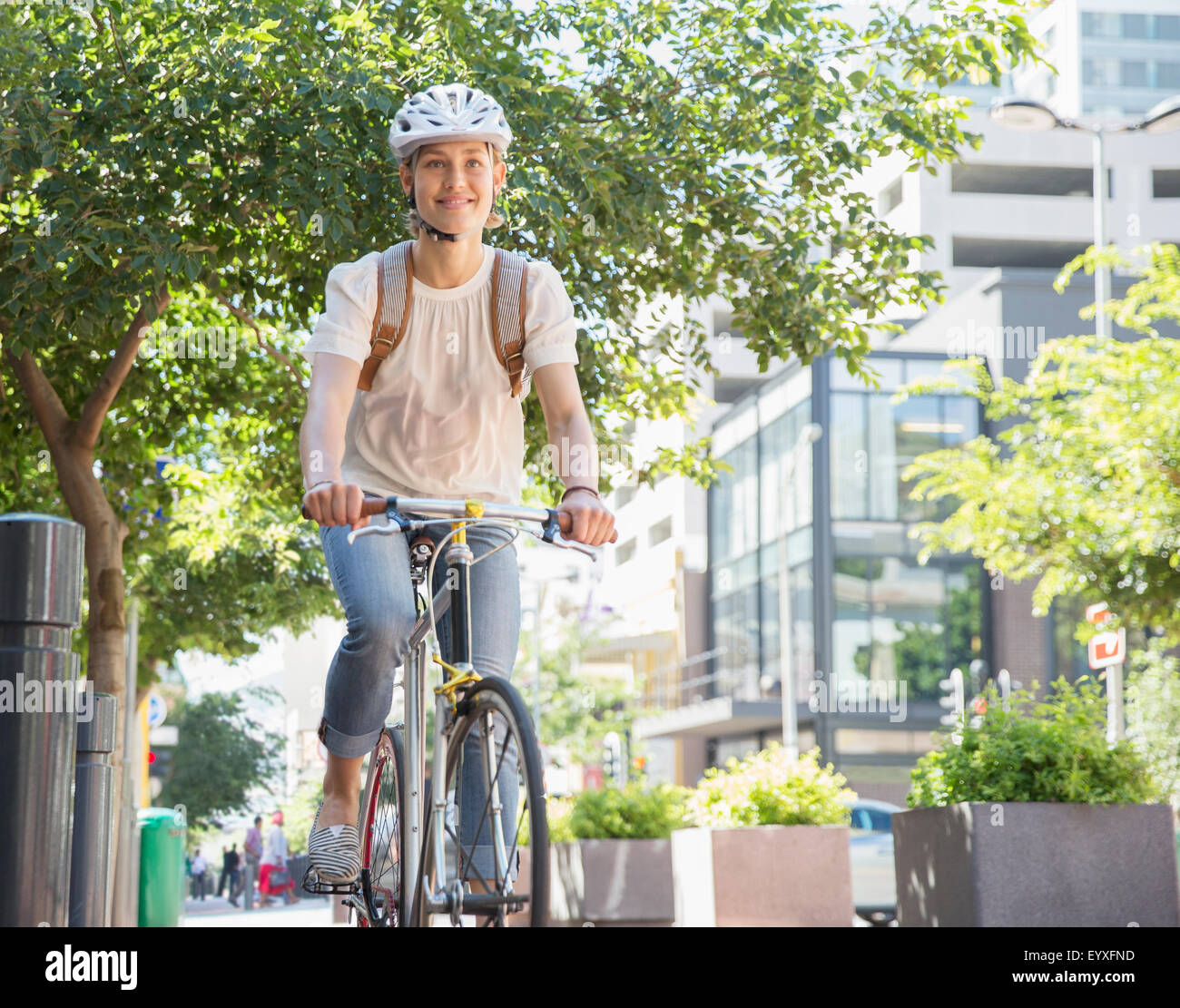 Portrait smiling young woman in helmet riding bicycle in urban park Stock Photo